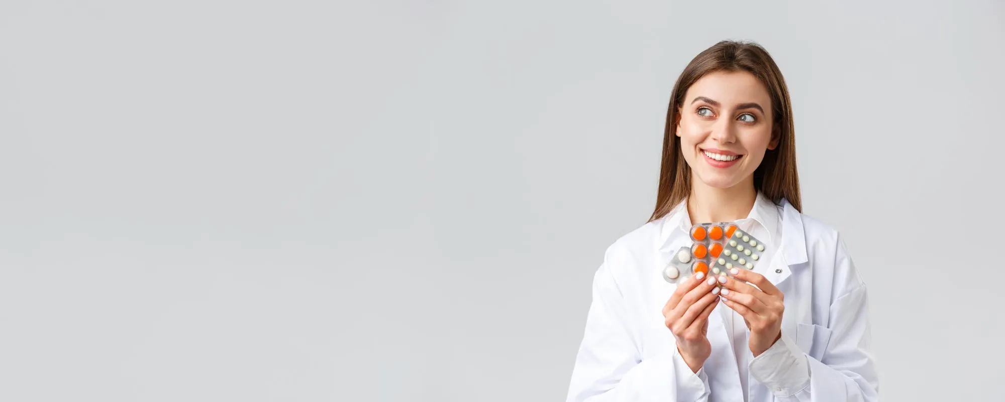 A female pharmacist or doctor with dark hair wearing a white lab coat and stethoscope carefully examining a small glass jar filled with yellow tablets, holding the cork lid in her other hand a detail-oriented approach to reviewing pill packs and medication dispensing at a professional pharmacy.