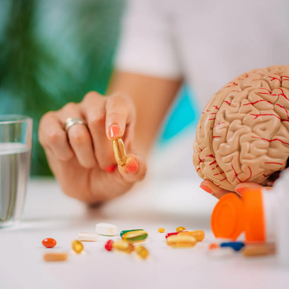 Person holding a vitamin supplement beside a brain model, representing Vitamins And Supplements Jacksonville.
