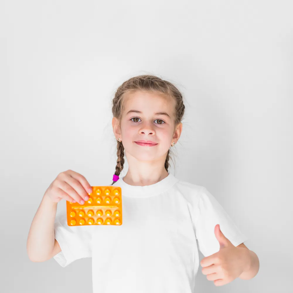 Child holding a blister pack of medication with a thumbs-up, representing safe and easy-to-use medicine packaging designed for better adherence and patient confidence