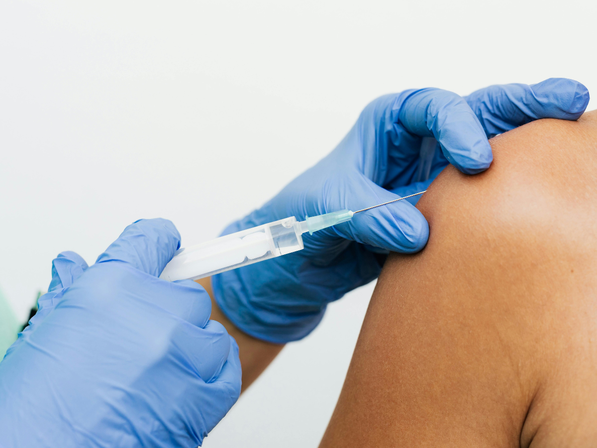 Healthcare professional wearing blue gloves administering a vaccine injection into a patient’s upper arm as part of immunizations services in a clean clinical setting.