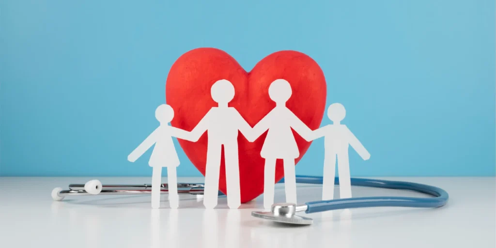 Wellness concept showing a family paper cutout holding hands in front of a red heart with a stethoscope, symbolizing family health and care.