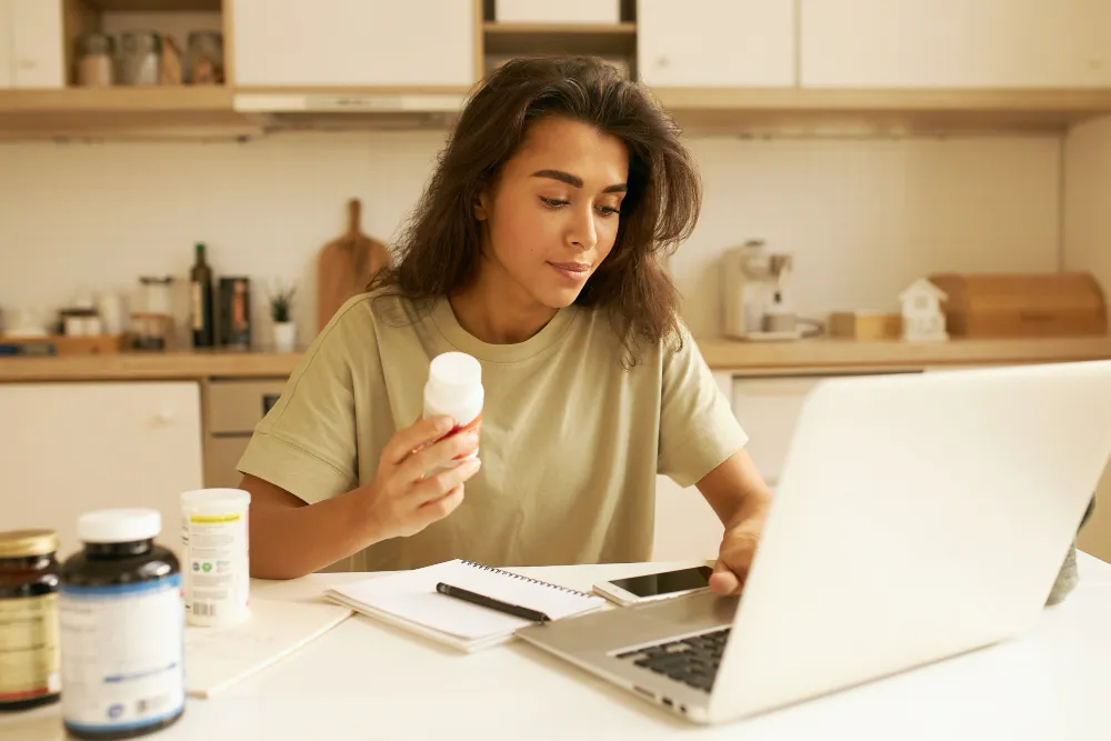 A woman organizing medications while working on a laptop, highlighting convenient and tech-enabled medication sync solutions and personalized medication management