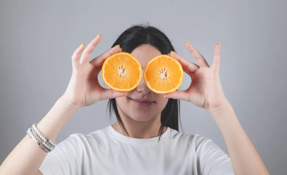 Woman holding orange slices over her eyes, symbolizing natural nutrition and the benefits of shopping at health food stores in Jacksonville Florida for fresh, vitamin-rich options