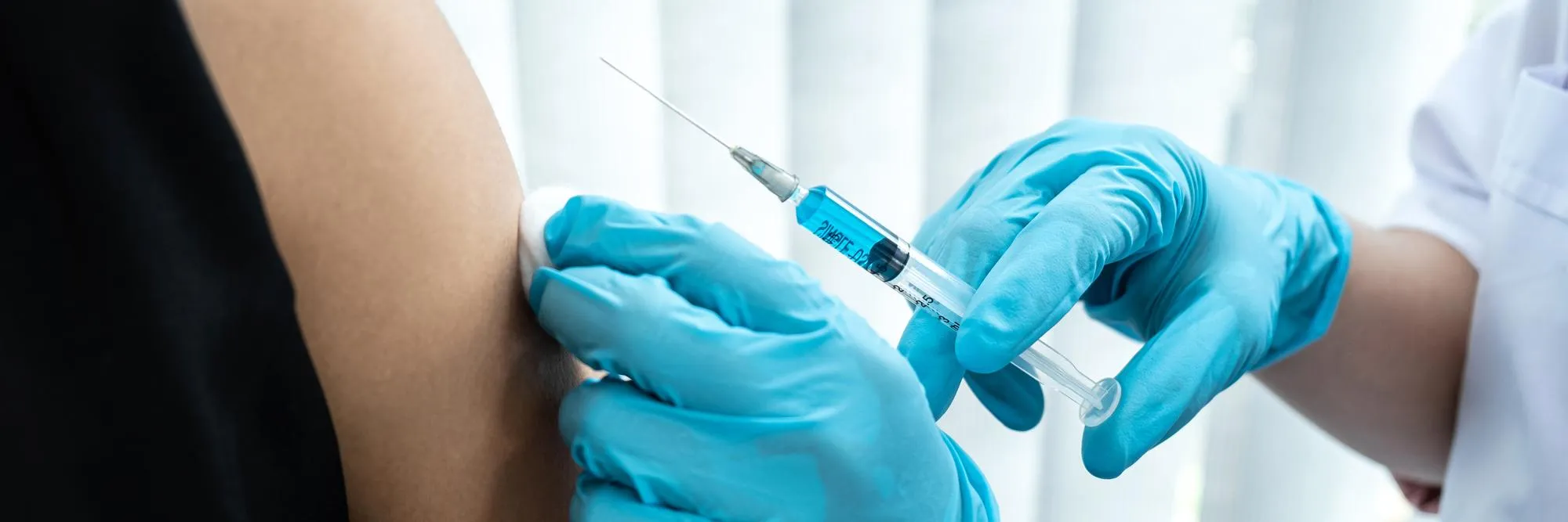 Healthcare worker in blue gloves administers a vaccination in the upper arm, injecting a patient.