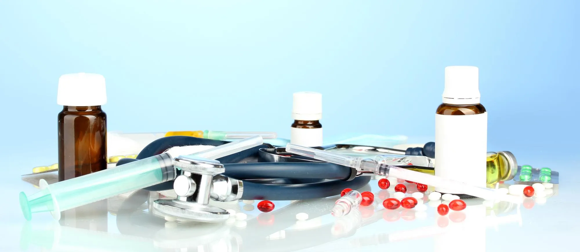Medical equipment including a stethoscope, syringe, prescription bottles, diagnostic tools, and healthcare supplies arranged on a clean surface, representing essential products available at a medical supply store for home and clinical care.