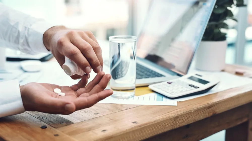 Patient taking prescribed medication with water at a desk, representing Med Sync solutions that coordinate refill schedules and improve medication adherence.