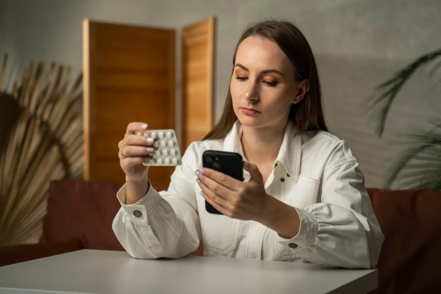 Person checking a medication blister pack on a smartphone, representing medication synchronization services that help patients manage refill schedules and stay on track with prescriptions.