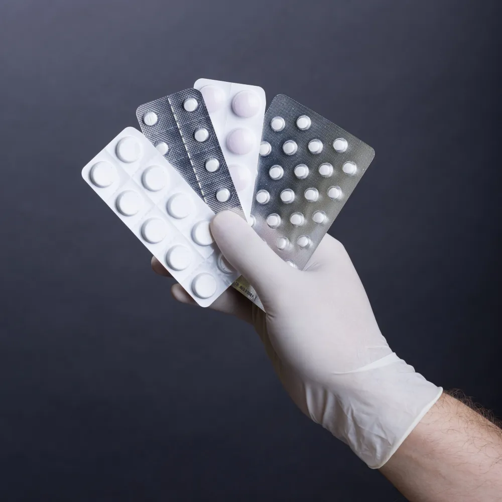 Gloved hand holding multiple medication blister packs, representing medical blister packaging services for safe and organized daily medication use.